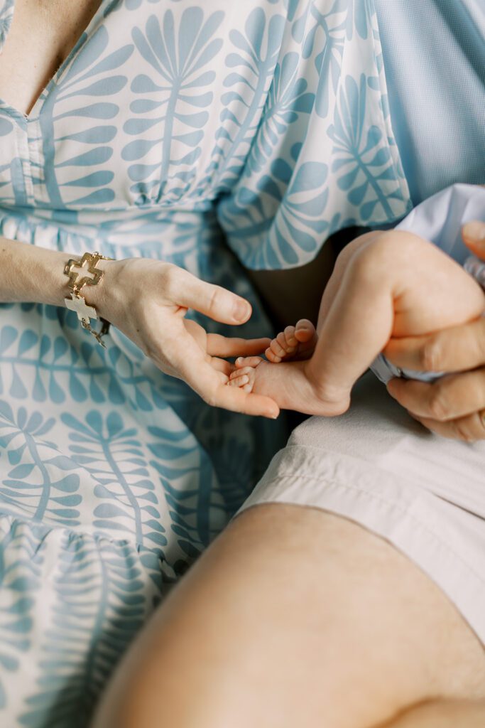  A mom wearing a blue dress holds her baby's feet during an at-home newborn photography session.